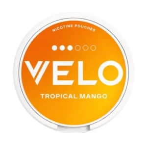 A direct top-down studio shot of a circular white can of Velo Tropical Mango Snus. The lid features a radiant gradient background transitioning from sunny yellow to deep orange, visually capturing the invigorating burst of tropical flavours and the lush sweetness of ripe mango described in the article. The brand name "VELO" stands out in large, bold white typography across the centre. Above the logo, a strength indicator displays three solid white dots followed by three outlined circles, visually confirming the product's moderate intensity. Below the branding, the text "TROPICAL MANGO" is printed in white capital letters, reinforcing the blend of mango with zesty notes of mandarin and passionfruit found within the nicotine pouches.